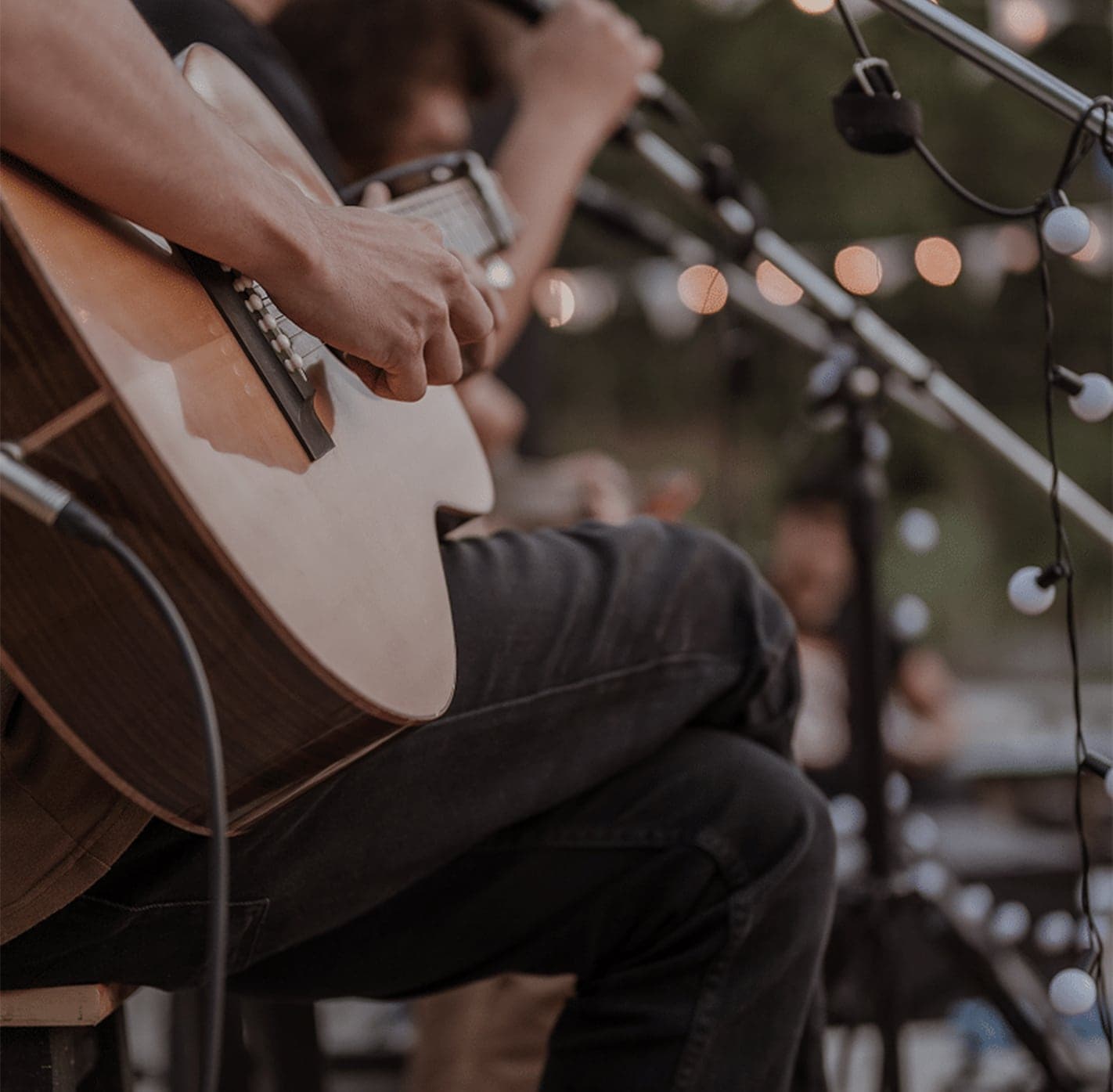 A man playing a guitar on a stage at night with lights in the background